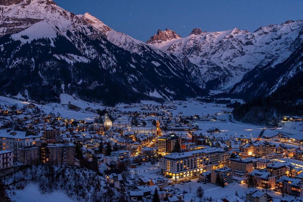 a city lit up in the snow at night with mountains at Hotel Waldegg - Adults only in Engelberg