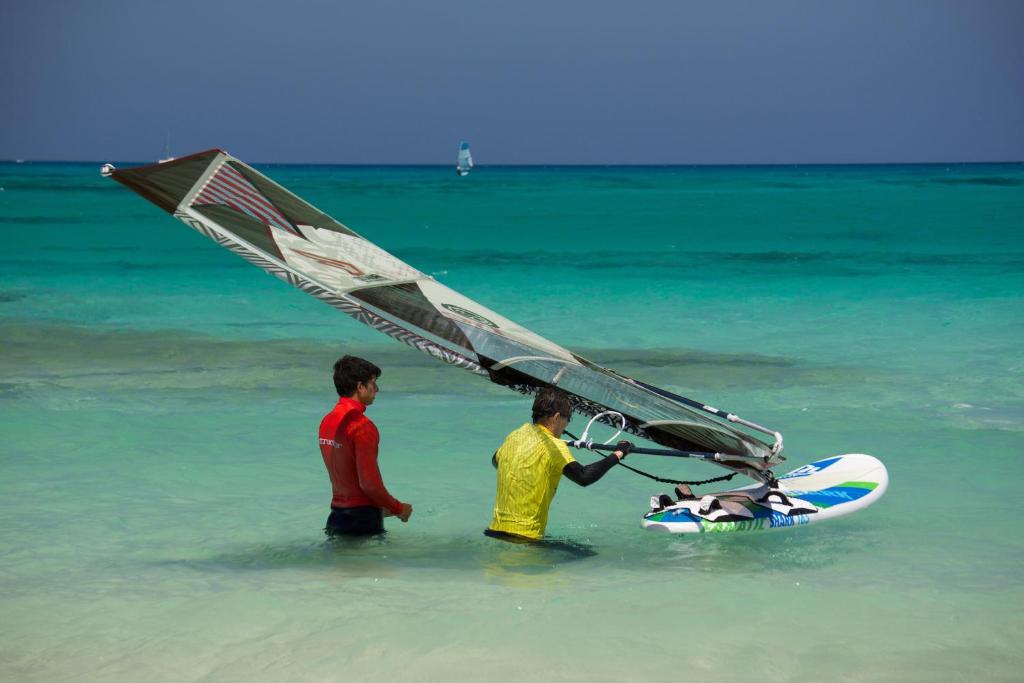 two men standing in the ocean with a sail on a surfboard at Surfers Retreat in Corralejo