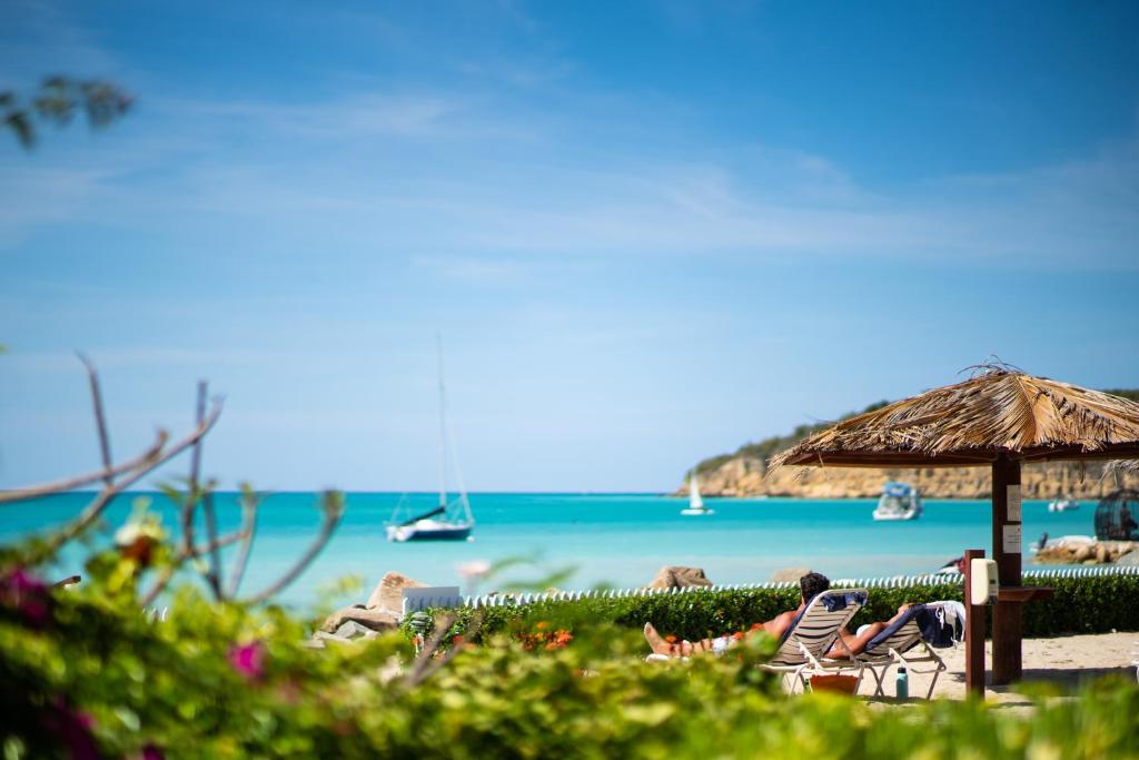 a beach with chairs and an umbrella and the ocean at Antigua Village Beach Resort in Saint Johnʼs