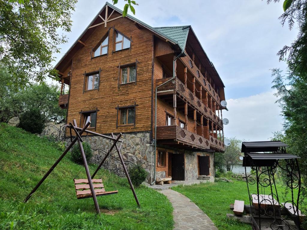 une grande maison en bois avec une aire de jeux en face de celle-ci dans l'établissement Гуцульська хата, à Yaremtche