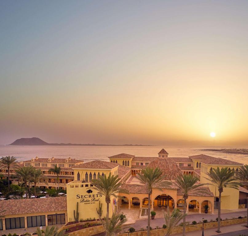 a view of a resort with palm trees and the sunset at Secrets Bahía Real Resort & Spa Adults only in Corralejo