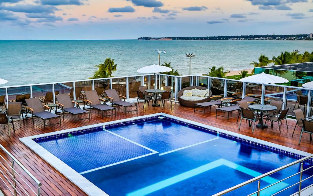 een balkon met een zwembad en stoelen en de oceaan bij Laguna Praia Hotel in João Pessoa