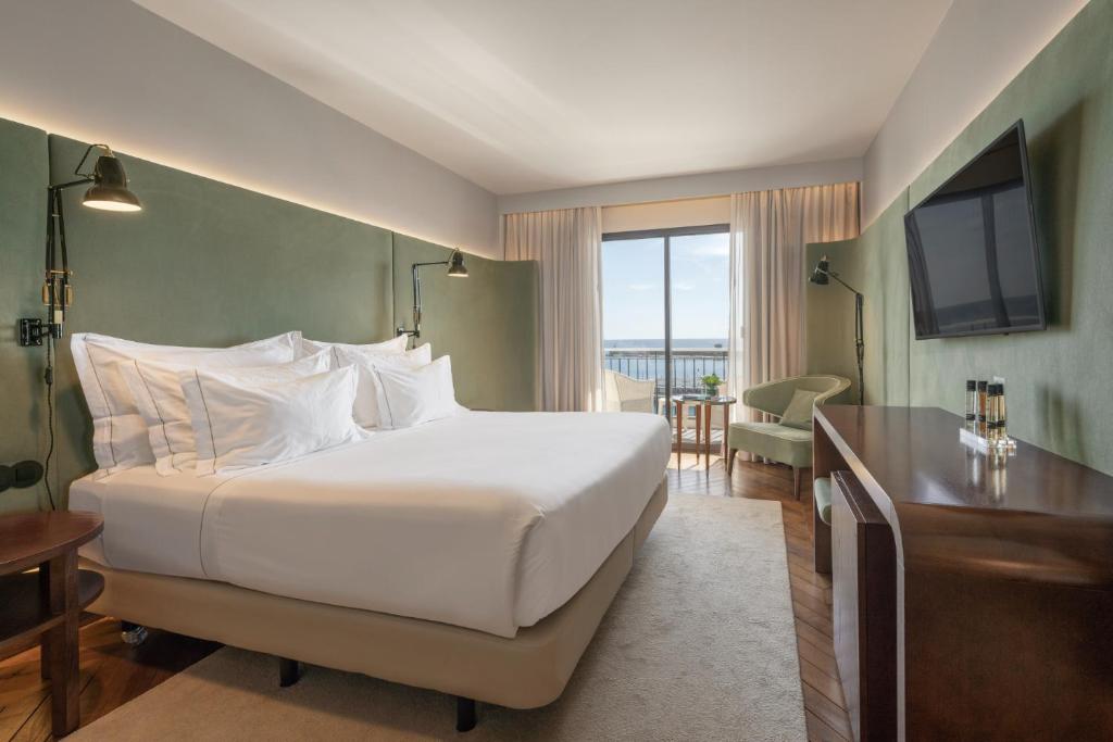 una camera da letto con un grande letto bianco e una televisione di Grand Hotel Açores Atlântico a Ponta Delgada