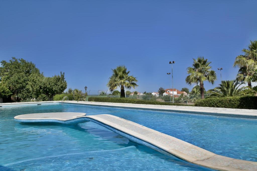 a swimming pool with blue water and palm trees at Turim Club Azeitao Hotel in Setúbal