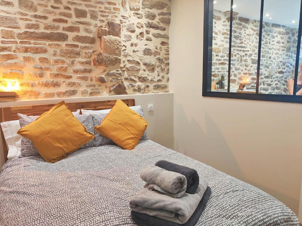 1 dormitorio con 1 cama con almohadas amarillas y pared de ladrillo en Appart Halo et Duplex Les Filles, en Dinan