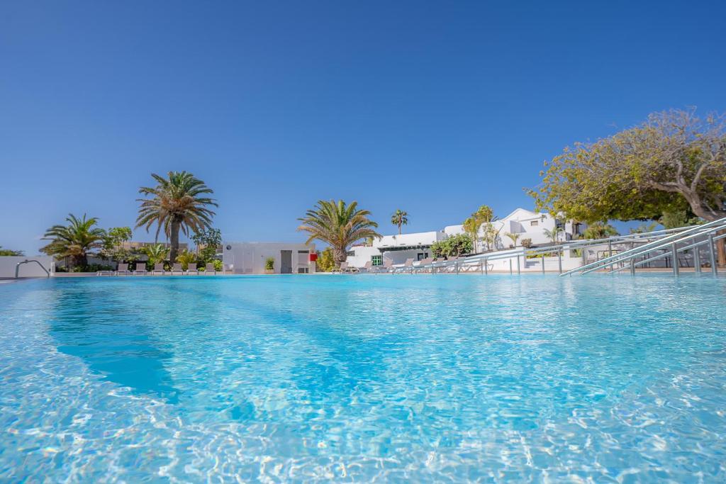 a large swimming pool with blue water and palm trees at Casas Heddy, Well-being Resort in Puerto del Carmen