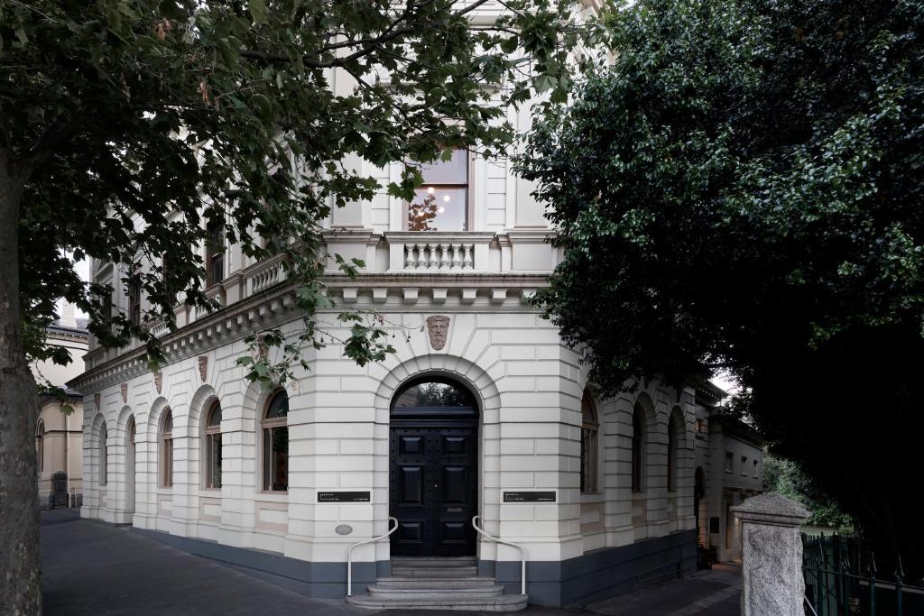 ein weißes Backsteingebäude mit einer schwarzen Tür in der Unterkunft Hotel Ernest Bendigo in Bendigo