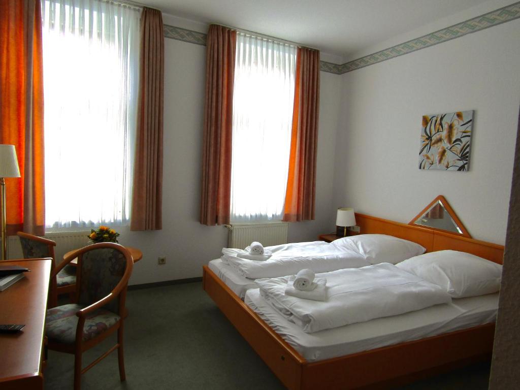 um quarto com 2 camas, uma cadeira e janelas em Pension Hexenkessel em Wernigerode