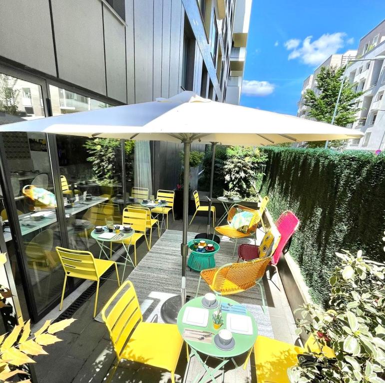 eine Terrasse mit Tischen, Stühlen und einem Sonnenschirm in der Unterkunft Residhome Asnieres Park in Asnières-sur-Seine