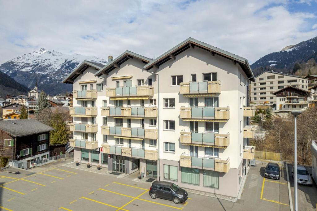 an apartment building in a parking lot with mountains in the background at Romatika 2 in Fiesch