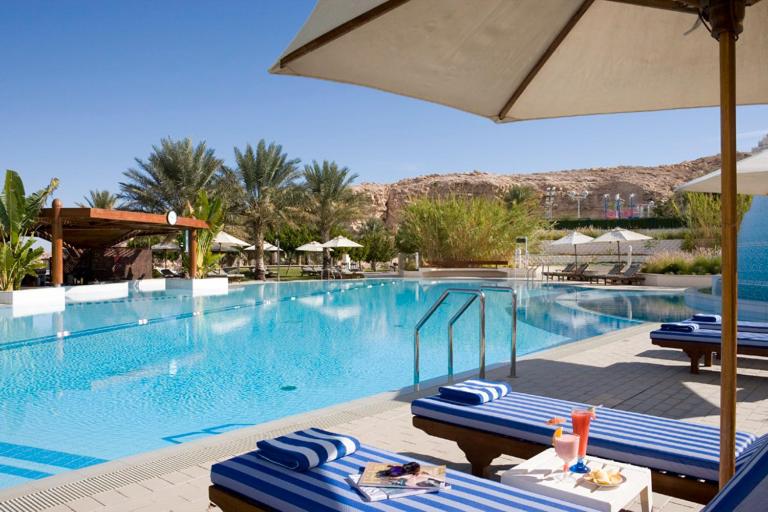 una piscina con sedie blu e bianche e ombrellone di Mercure Grand Jebel Hafeet Hotel a Al Ain