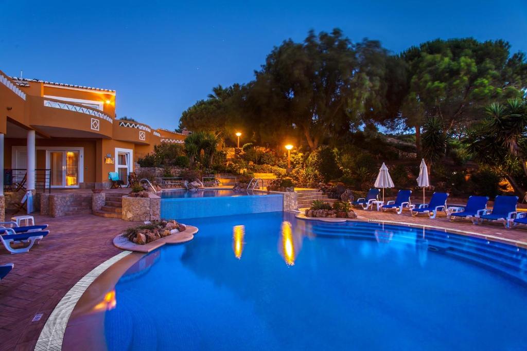 uma piscina à noite com cadeiras e guarda-sóis em Montinho De Ouro na Praia da Luz