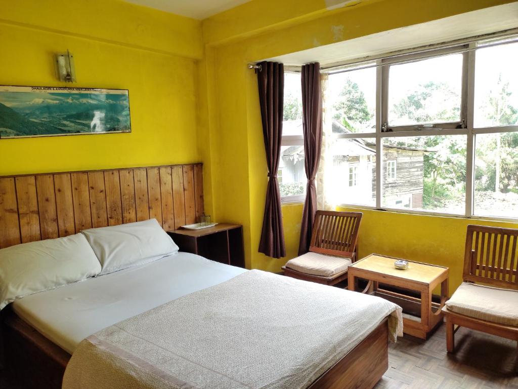 een slaapkamer met een bed en 2 stoelen en een raam bij Hotel Mhelung in Darjeeling