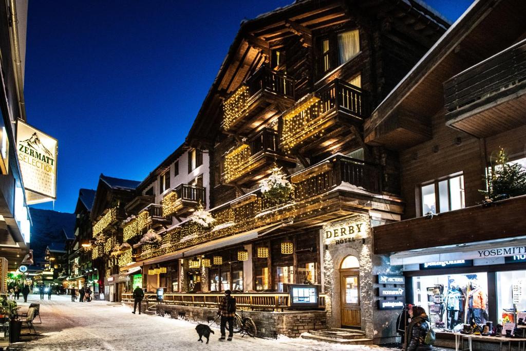 una calle de la ciudad con gente paseando a un perro delante de un edificio en Hotel Derby, en Zermatt