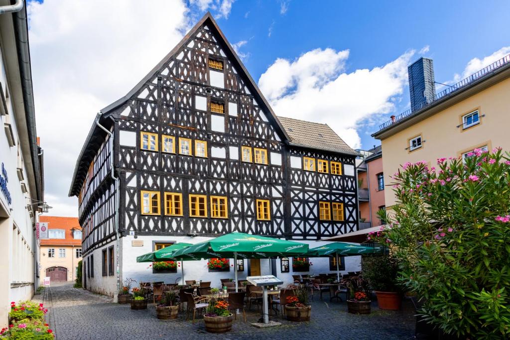 un ancien bâtiment noir et blanc avec des tables et des parasols dans l'établissement Watzdorfer Geleitschenke und Herberge, à Weimar