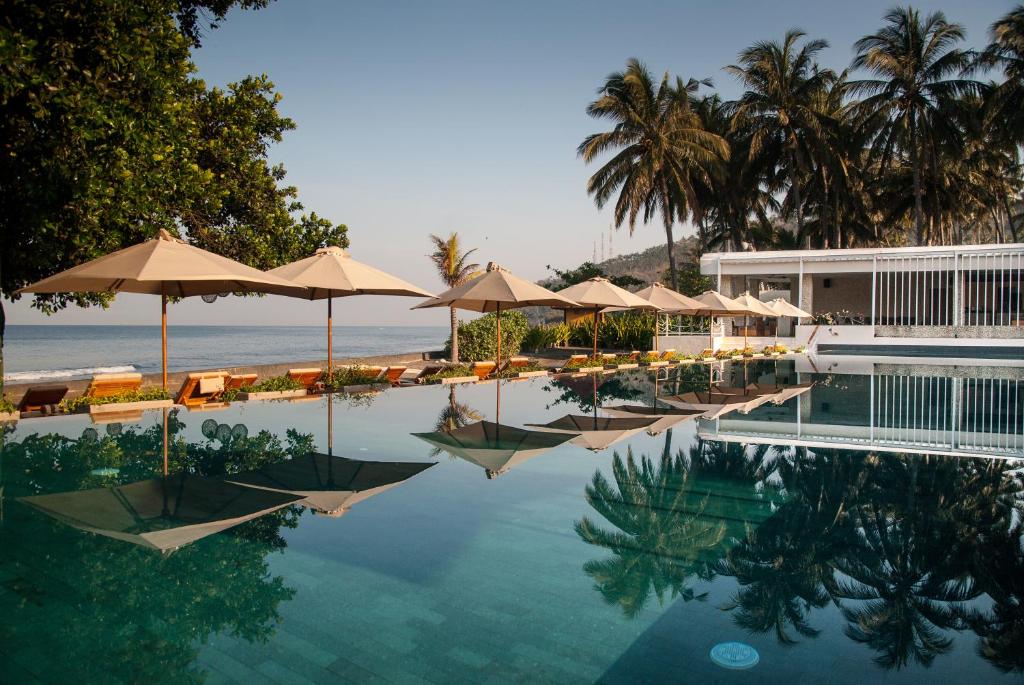 a swimming pool with umbrellas and chairs and the ocean at Living Asia Resort and Spa in Senggigi 