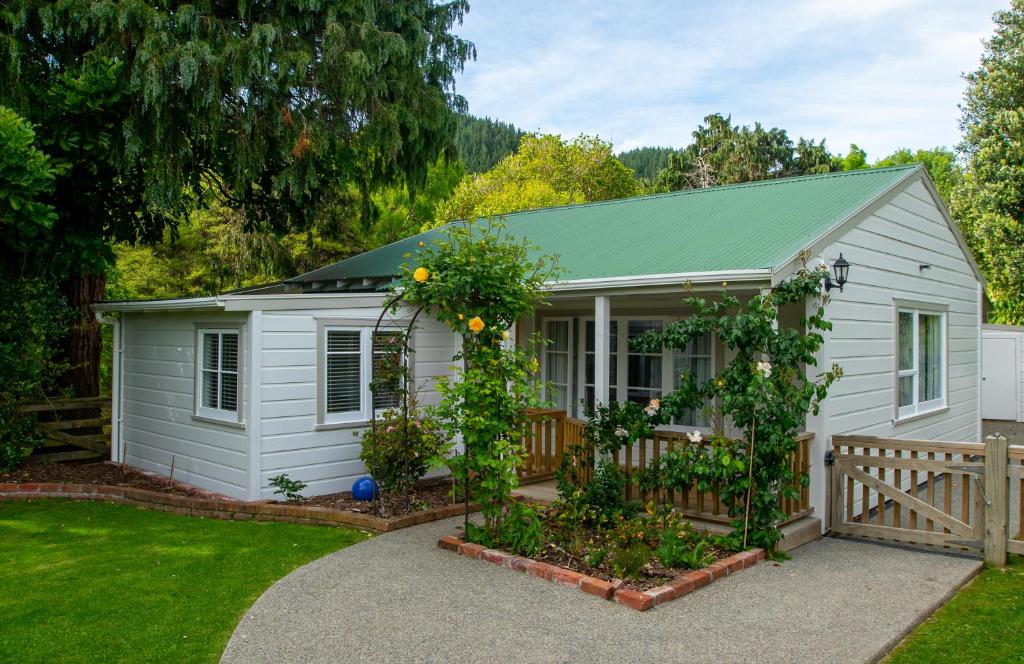 einen kleinen weißen Schuppen mit einem Zaun und einem Garten in der Unterkunft Birdsong Cottage in Paraparaumu