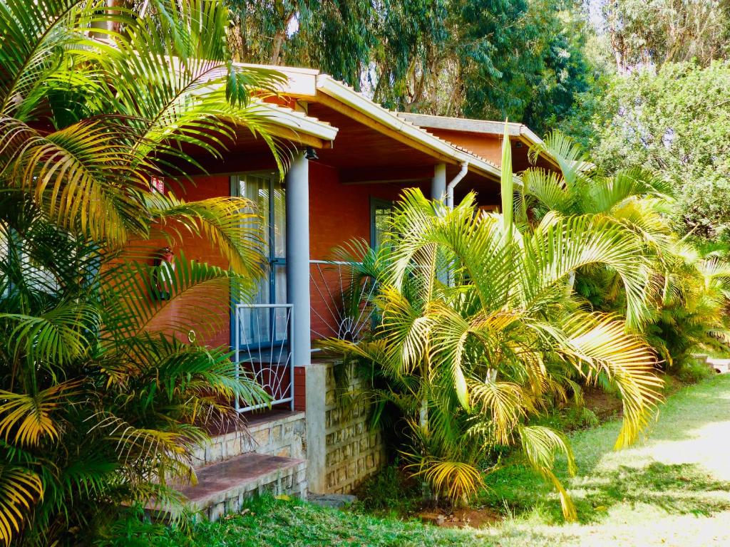 une maison rouge avec des palmiers devant elle dans l'établissement Le Chat'o Park Hotel Ivato Airport NAVETTE GRATUITE H24, à Antananarivo