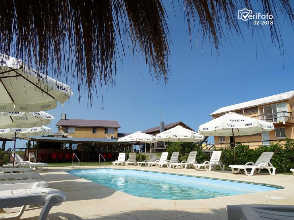 einen Pool mit weißen Stühlen und Sonnenschirmen in der Unterkunft Hotel Aquarella in Punta Del Diablo