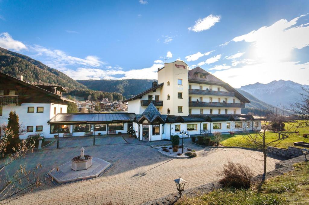 un grand bâtiment avec une cour et des montagnes en arrière-plan dans l'établissement Smy Koflerhof Wellness & Spa Dolomiti, à Rasun di Sopra