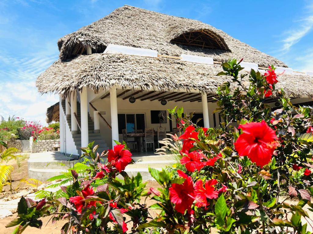 dom z dachem krytym strzechą i czerwonymi kwiatami w obiekcie Beba.Beach.House w mieście Watamu