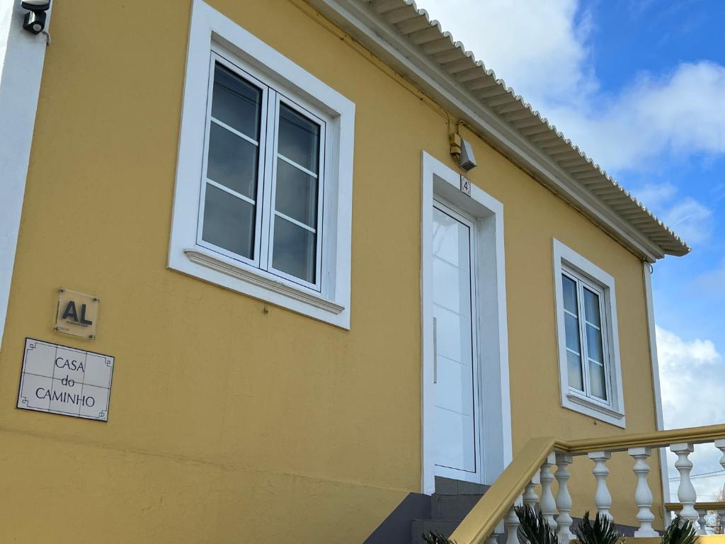 une maison jaune avec une porte blanche et un panneau dans l'établissement CASA do CAMINHO, à Praia da Vitória