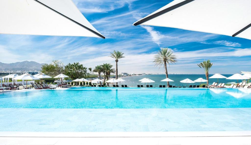 una gran piscina con palmeras y sombrillas en Crowne Plaza Muscat, an IHG Hotel, en Mascate