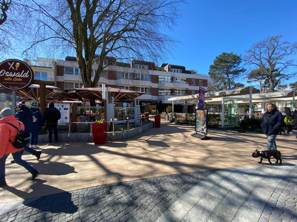 Ein Mann und ein Hund laufen auf einem Bürgersteig in der Unterkunft Modernes Apartment an Timmendorfer Promenade, 1. Reihe in Timmendorfer Strand