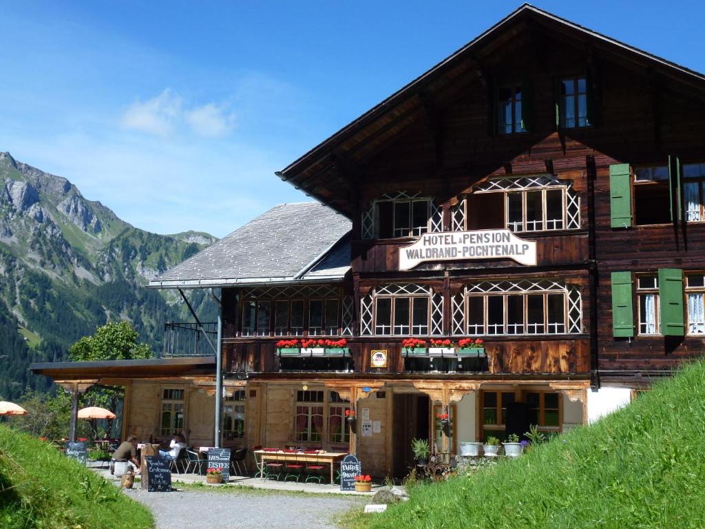 ein großes Holzgebäude mit Leuten, die davor sitzen in der Unterkunft Hotel Waldrand in Kiental