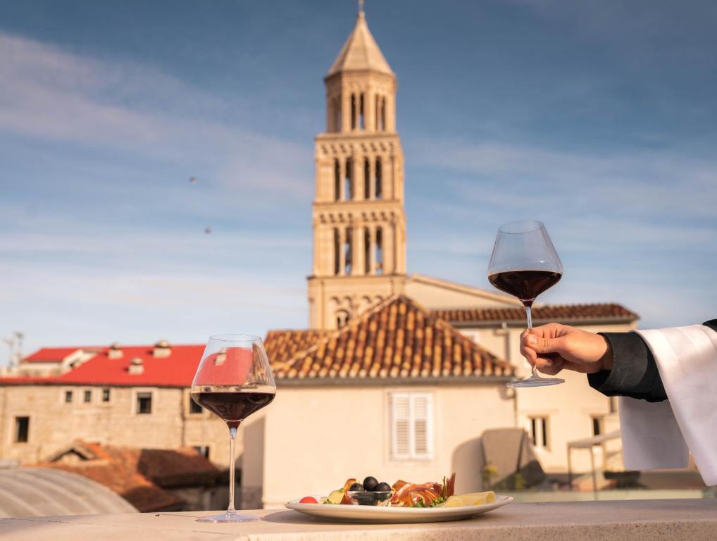 a person holding a glass of wine next to a plate of food at Slavija Culture Heritage Hotel in Split