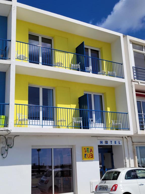 un edificio amarillo con balcones azules y un coche aparcado delante en Seakub hotel, en Royan