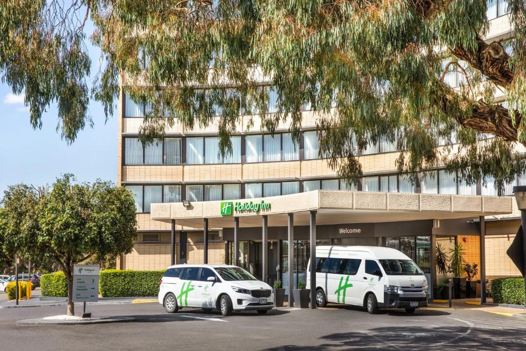 dois veículos brancos estacionados em frente a um edifício em Holiday Inn Melbourne Airport, an IHG Hotel em Melbourne