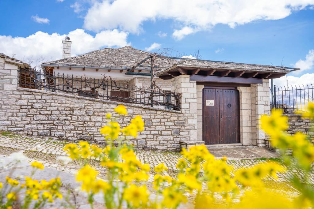 uma casa de tijolos com uma porta de madeira e flores amarelas em Zagori Home em Monodendri