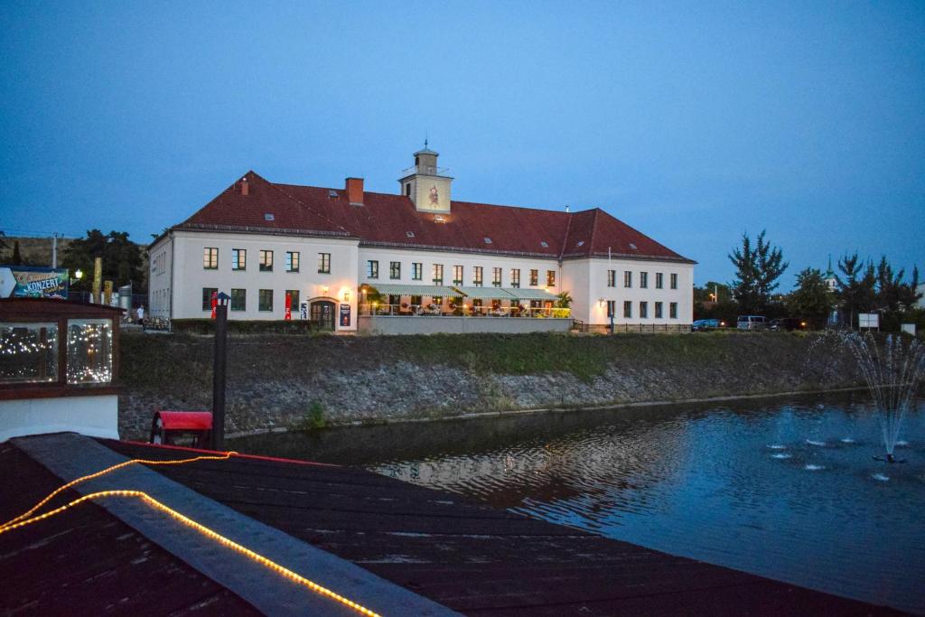 un grand bâtiment blanc à côté d'une étendue d'eau dans l'établissement Restaurant und Pension Alberthafen, à Dresde