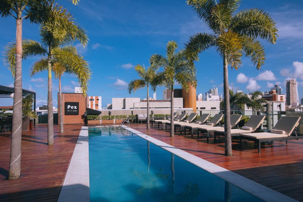 een zwembad met ligstoelen en palmbomen op een gebouw bij LS Hotel in João Pessoa