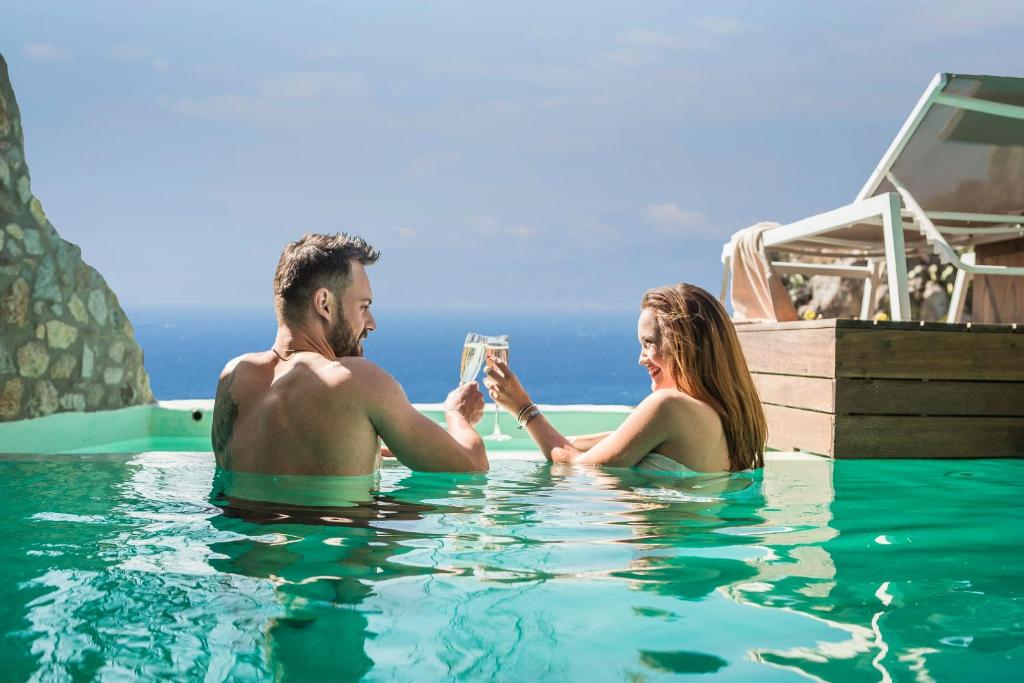 een man en vrouw in een zwembad met een glas wijn bij KLIDON Dreamy Living Suites in Mykonos-stad