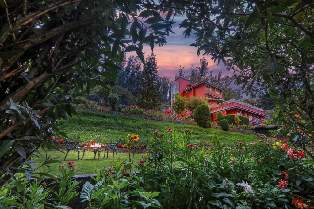 een tuin met bloemen en een rood huis op de achtergrond bij Willow Hill by Nature Resorts in Ooty