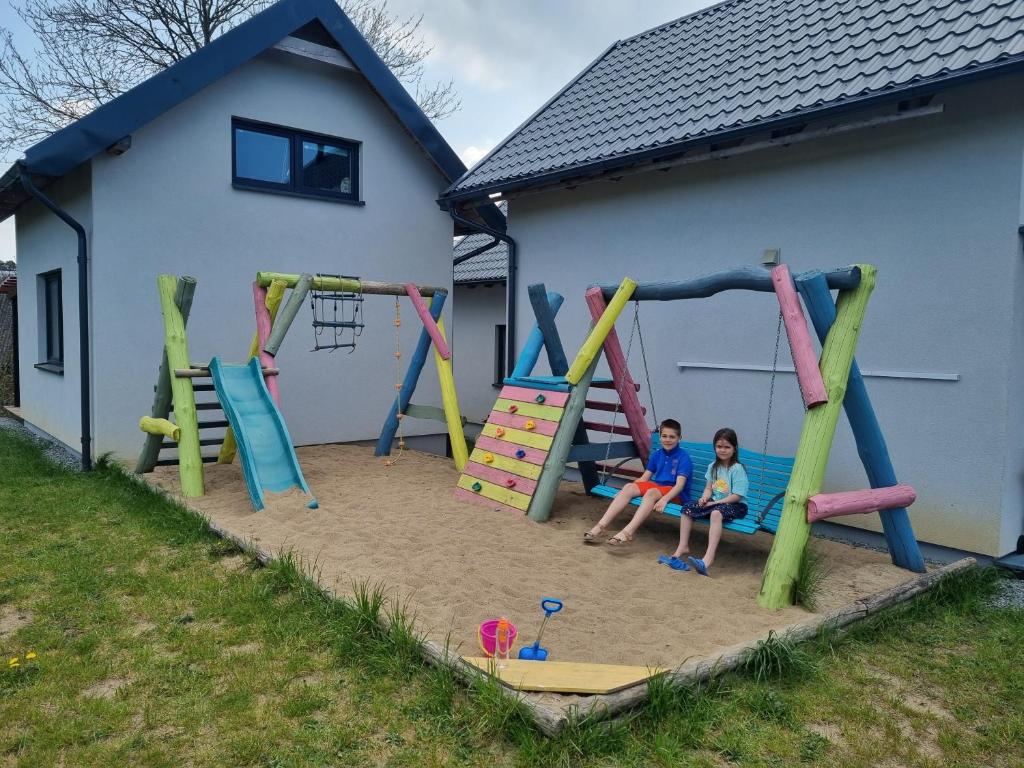 2 enfants assis sur une aire de jeux dans le sable dans l'établissement Domki na Wzgórzu Jastrzębia Góra Tupadły, à Jastrzębia Góra