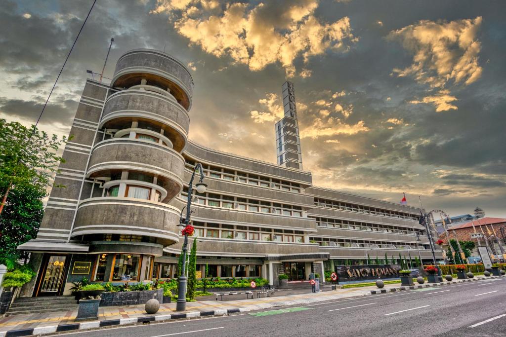 ein großes Gebäude auf einer Stadtstraße mit wolkigem Himmel in der Unterkunft Hotel Savoy Homann in Bandung