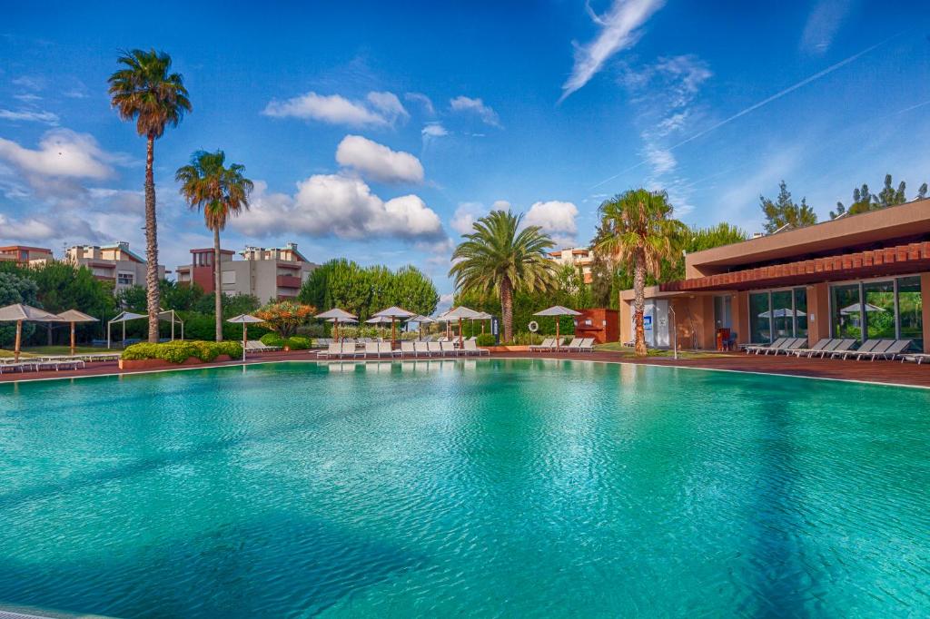 una grande piscina con palme e un edificio di Aqualuz Troia Mar by The Editory a Tróia