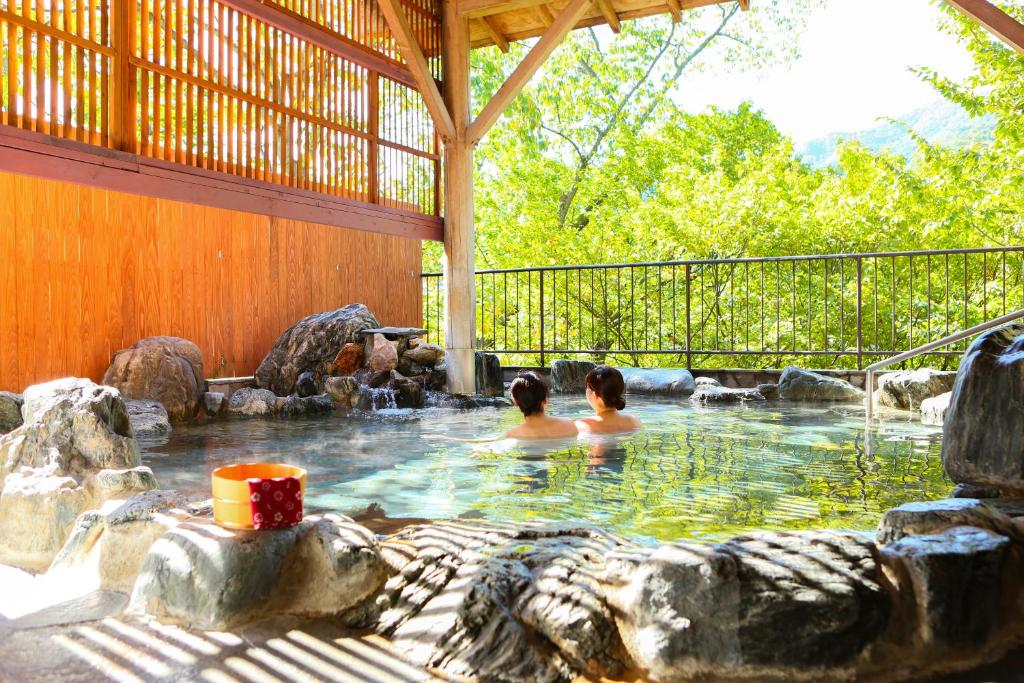 duas pessoas numa banheira de hidromassagem num quintal em Ooedo Onsen Monogatari Hotel Kinugawa Gyoen em Nikko