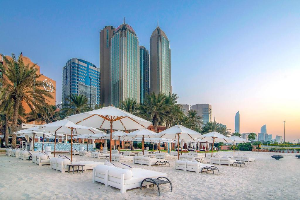 una spiaggia con sedie e ombrelloni bianchi e edifici di Sheraton Abu Dhabi Hotel & Resort a Abu Dhabi