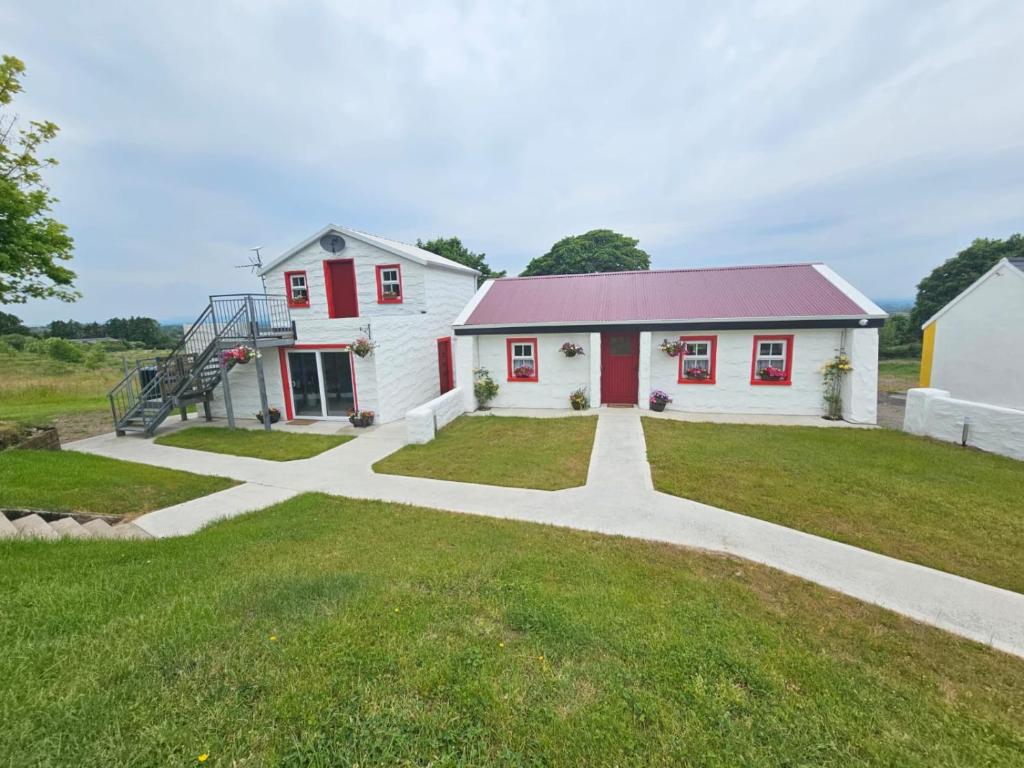 une maison blanche avec des portes rouges et une pelouse dans l'établissement Tiernan's Luxury Cottages, à Charlestown