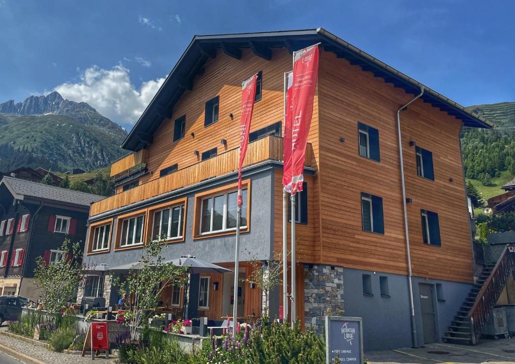 een groot houten gebouw met vlaggen ervoor bij Mountain Lodge Sedrun in Sedrun