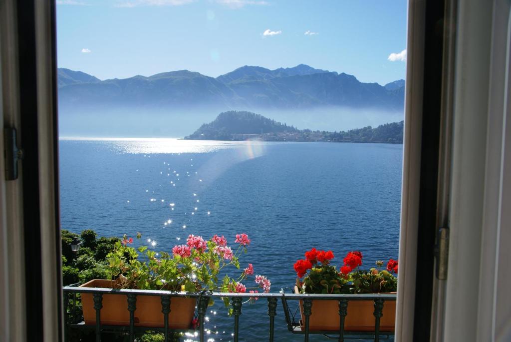 een uitzicht op het water vanuit een raam met bloemen bij Hotel Riviera in Griante Cadenabbia