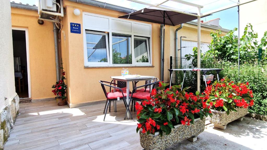 un patio con mesa, sillas y flores rojas en Apartment Jagoda, en Krk