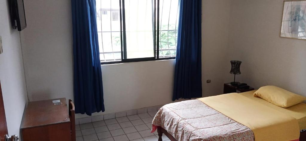 a bedroom with a bed and a window with blue curtains at Hostal Iberia in Talara