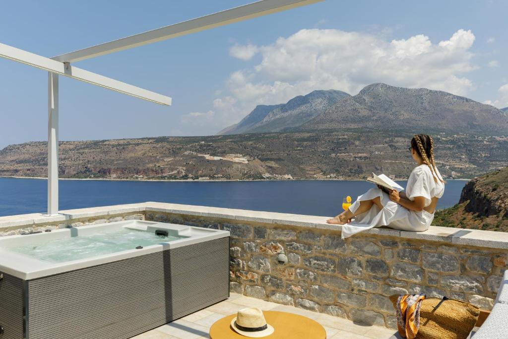 a woman sitting on a wall reading a book next to a bath tub at Trapela Limeni Luxury Suites in Limeni