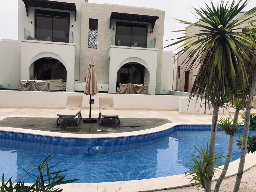 ein Haus mit einem Pool mit zwei Stühlen und einem Sonnenschirm in der Unterkunft Rivira Miko 2 in Salalah