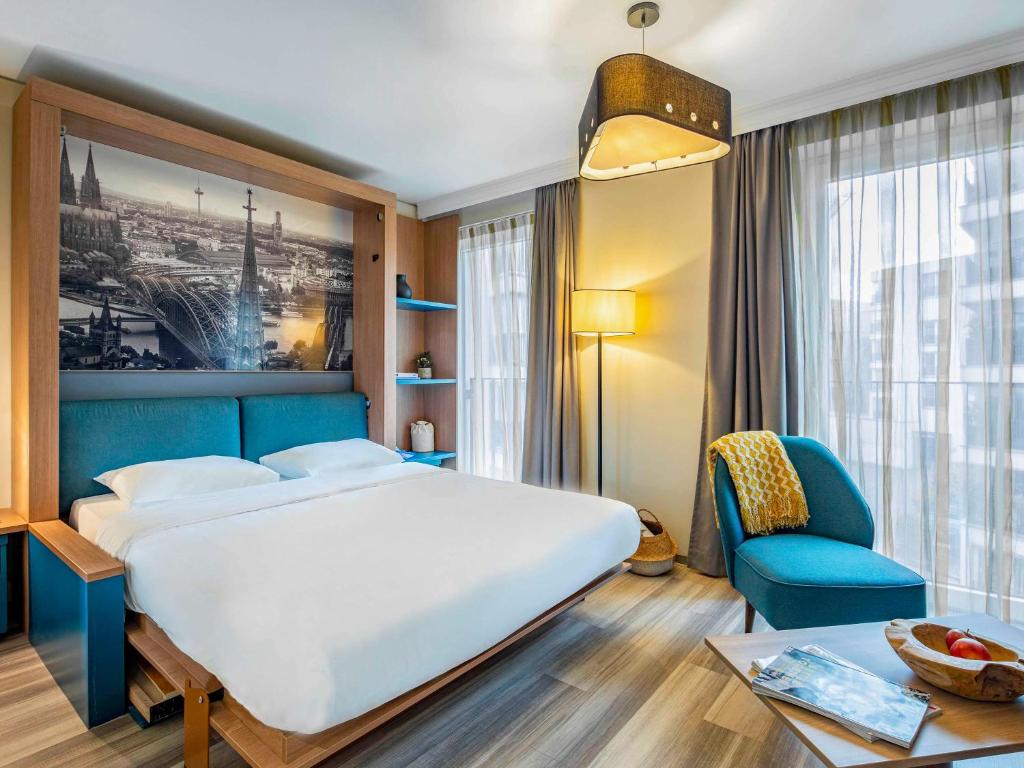 a bedroom with a large bed and a blue chair at Aparthotel Adagio Köln City in Cologne